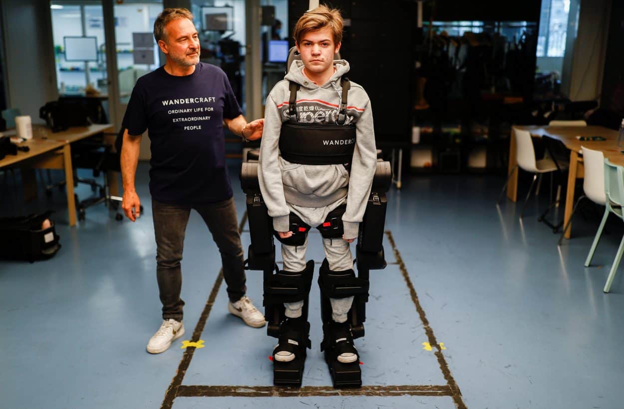 Jean-Louis Constanza helped his 16-year-old son Oscar using a robot exoskeleton at the company headquarters in Paris, France July 9, 2021. (Credit: REUTERS/Christian Hartmann)